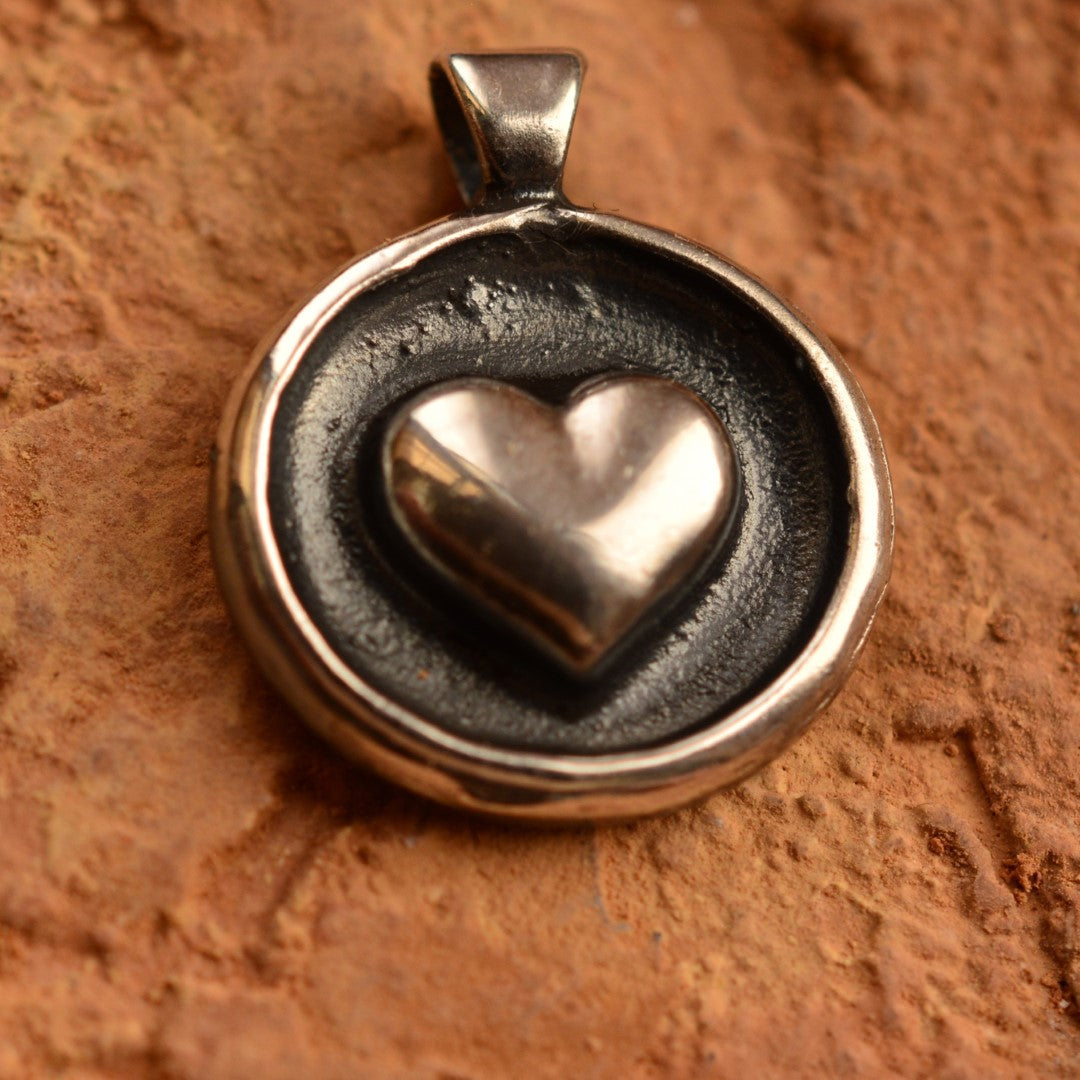 Сребърен медальон 925 с релефно сърце – ръчно изработен талисман за любов и закрила, бохо-рустик скулптурно бижу от Арт Дива, заснето върху каменен фон.