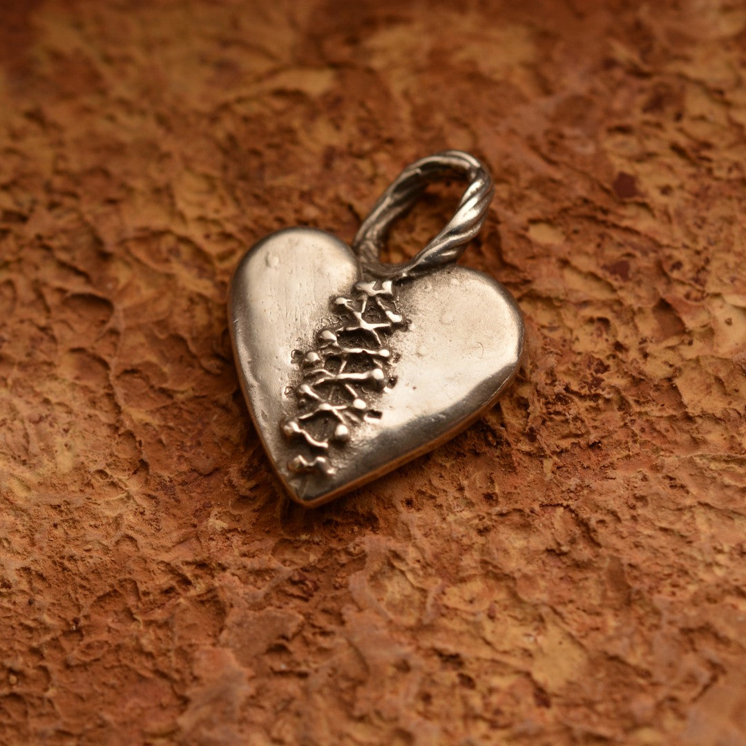 Сребърен медальон 925 „Закърпено сърце“ – ръчно изработен талисман и амулет на любовта и надеждата, бохо-рустик скулптурно бижу от Арт Дива, заснето върху каменен фон.