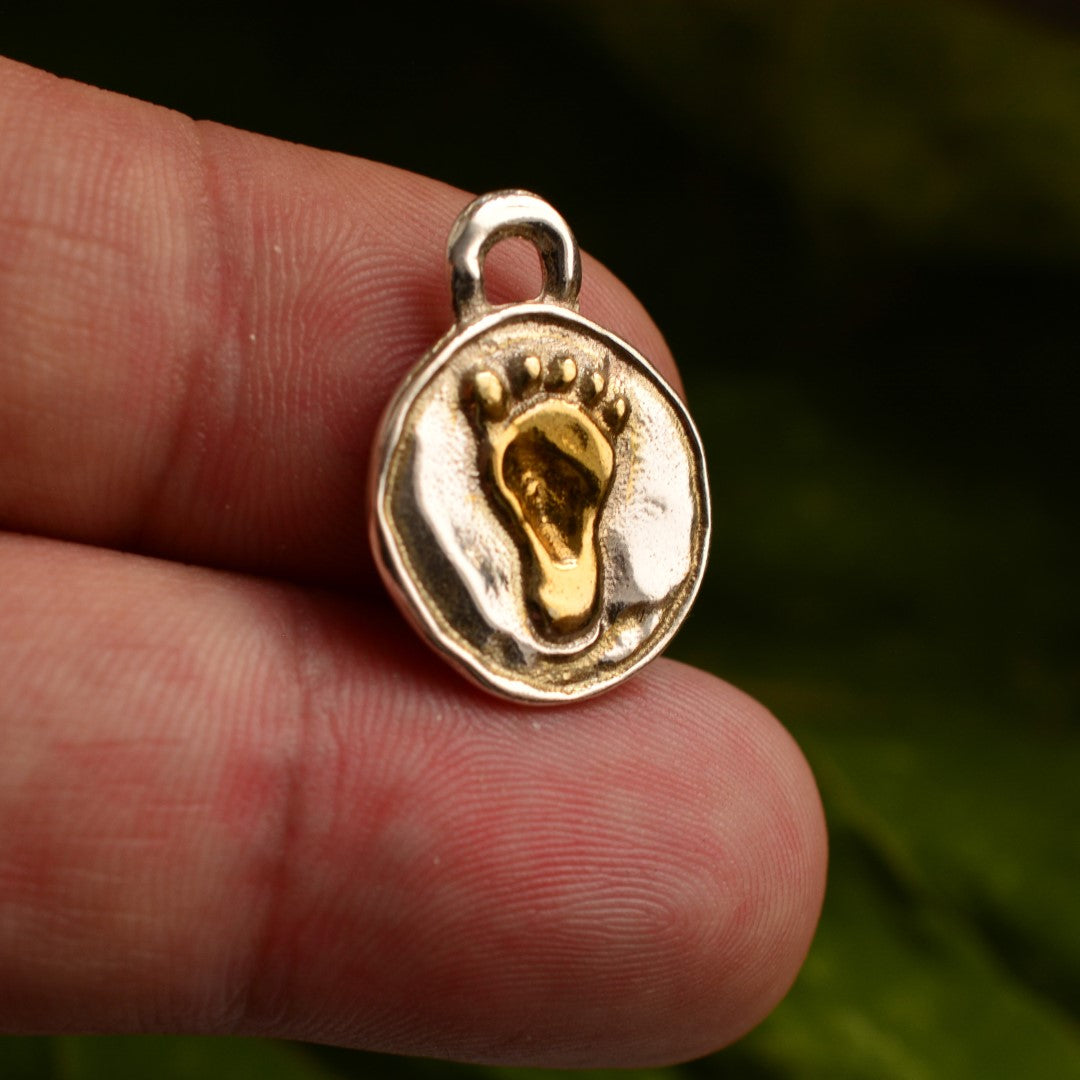 Ръчно изработен сребърен медальон 925 „Бебешко краче“ със златни акценти – амулет на майчината любов, новия живот и връзката между дете и родител, бохо-рустик скулптурно бижу от Арт Дива, заснето върху зелен натурален фон.
