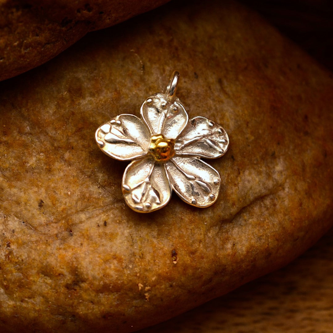 Сребърен медальон 925 „Черешов цвят“ със златни акценти – ръчно изработен талисман на пролетта, чистотата и новото начало, бохо-рустик скулптурно бижу от Арт Дива, заснето върху естествен каменен фон.
