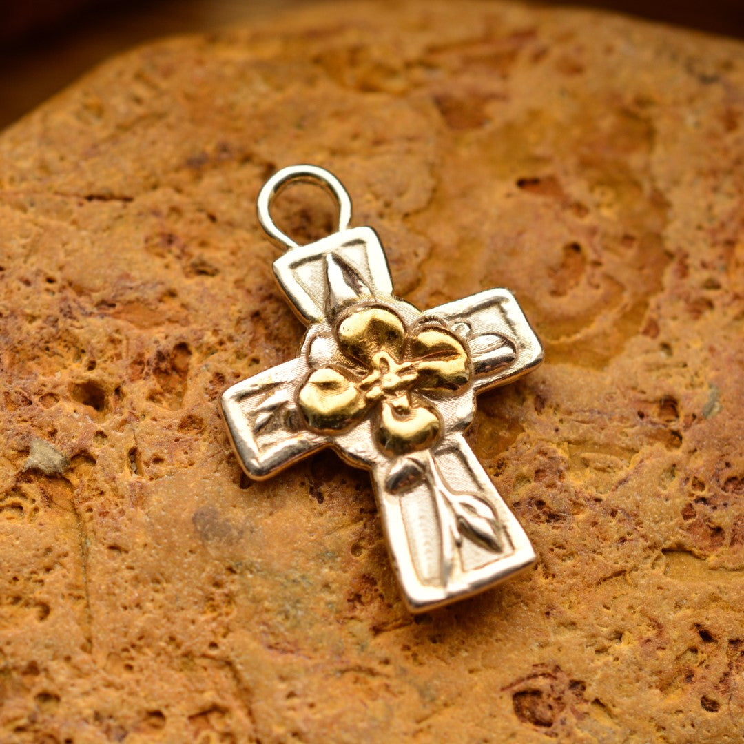 Сребърен медальон 925 „Кръст с цвете“ със златни акценти – ръчно изработен талисман на вярата, надеждата и новото начало, бохо-рустик скулптурно бижу от Арт Дива, заснето върху топъл каменен фон.

