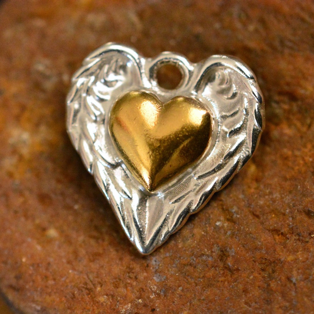 Сребърен медальон 925 със златен акцент „Сърце с ангелски крила“ – символ на любов и закрила, ръчно изработено бохо-рустик скулптурно бижу от Арт Дива, заснето върху кафяв камък.
